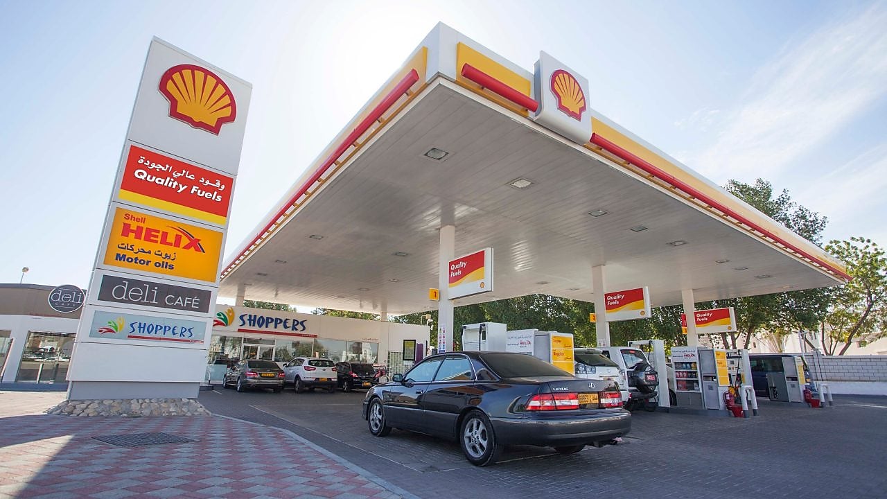 سيارة فيراري حمراء في الساحة الأمامية لمحطة شل مع رجل يستعد لتعبئتها بالبنزين