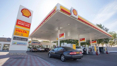 سيارة فيراري حمراء في الساحة الأمامية لمحطة شل مع رجل يستعد لتعبئتها بالبنزين