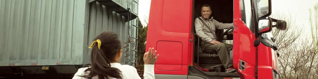 رجل في مقصورة شاحنة حمراء بابها مفتوح يلوح لابنته