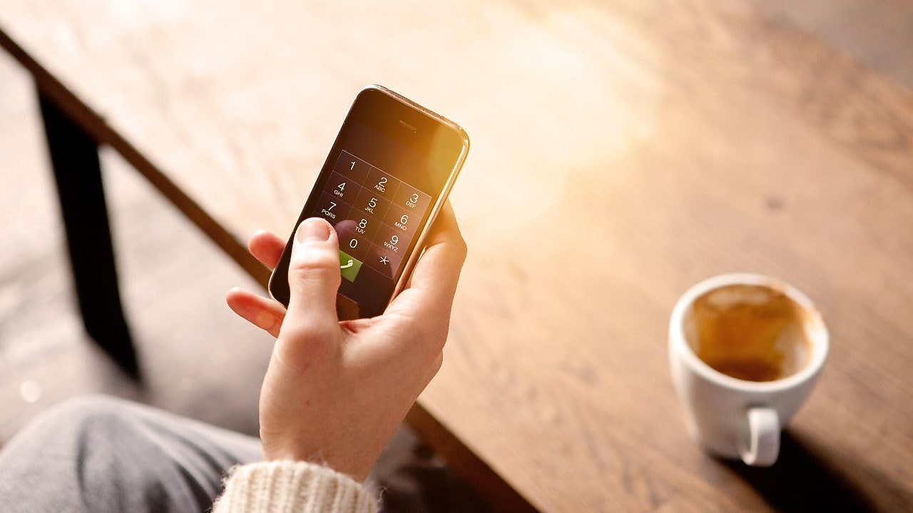 رجل يحمل هاتفًا نقالًا ويحتسي قهوة