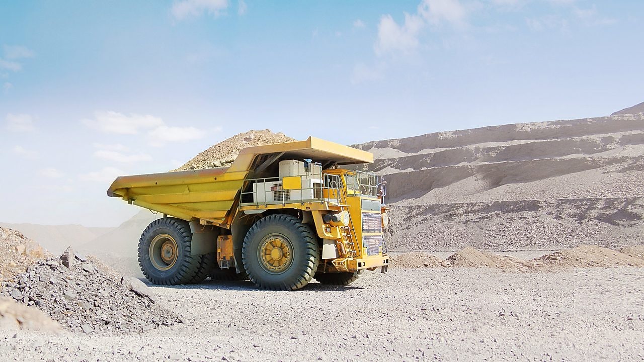 Yellow dumper truck driving through gravel