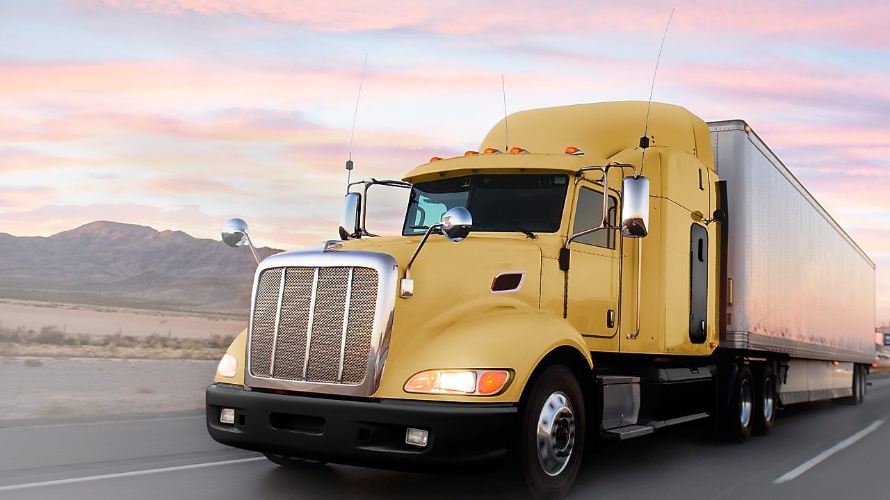 een gele truck die bij schemering over een weg rijdt