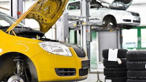 twee auto's in een garage, een gele en een witte, met hun motorkap open, en autobanden op de achtergrond