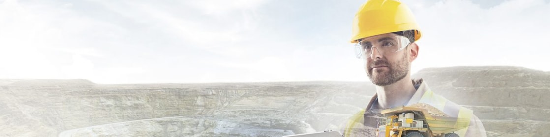 worker in yellow hard hat transposed onto a background of cliffs and a large yellow truck