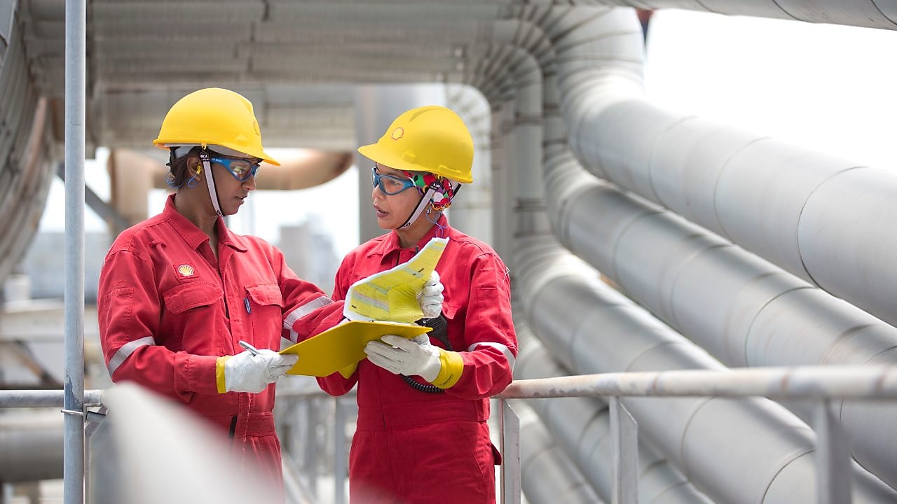 Shot of two workers in hardhats discussing a project in a refinery