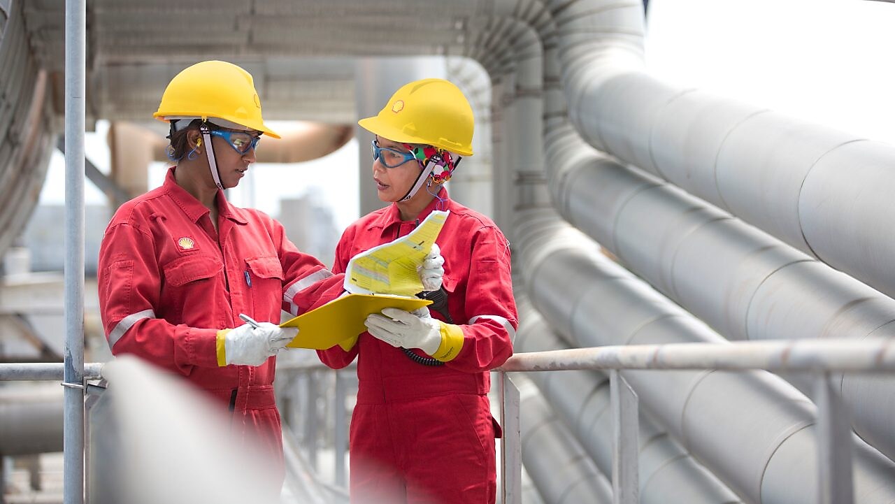 Shot of two workers in hardhats discussing a project in a refinery