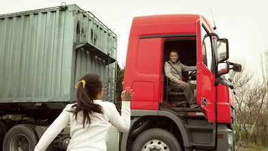 Man in red truck cab with door open waving to his daughter